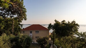 A house with a red roof, surrounded by greenery and overlooking a body of water. - Apartments Belenum - One-Bedroom Apartment with Balcony and Sea View (no.3) (Mlini)