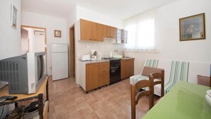 Una cocina compacta con armarios de madera, una mesa de comedor con sillas, un televisor y un refrigerador.