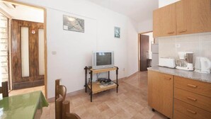 Una cocina compacta con armarios de madera, un televisor sobre un mueble bajo y una cafetera.
