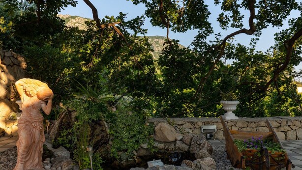 A garden with a statue, a stone wall, and a wooden planter. - Apartments Belenum - Comfort Double Room with Balcony and Sea View (no.1) (Mlini)