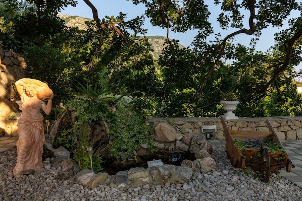 Un jardin agrémenté d’une statue, d’un mur en pierre et d’un bac à fleurs en bois.