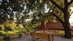 An outdoor patio with a wooden table set for dining, surrounded by benches, and a brick chimney structure. - Apartments Belenum - Comfort Double Room with Balcony and Sea View (no.1) (Mlini)