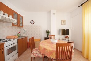 Eine kleine Küche mit Herd, Backofen und Holzschränken. Ein Esstisch mit Stühlen und ein an der Wand befestigter Fernseher sind ebenfalls vorhanden.