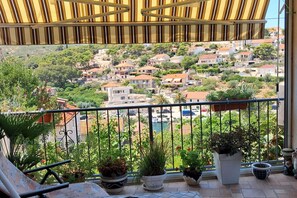 Un balcone con vista su una cittadina collinare, piante in vaso e una tenda da sole a righe.