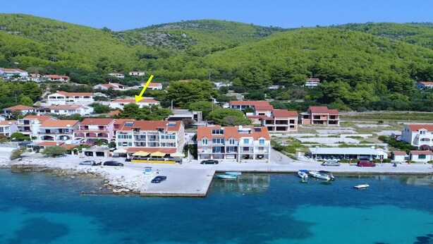 Un pueblo costero con edificios a lo largo del malecón, un puerto deportivo con barcos y un paisaje montañoso de fondo.