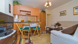 Ein kompakter Wohnraum mit Essbereich, einer Couch, einem Fernseher und einem kleinen Tisch mit Pflanze.