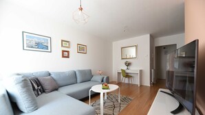 Una sala de estar moderna con un sofá gris, una mesa de centro blanca con fruta, un televisor de pantalla plana y obras de arte en las paredes.
