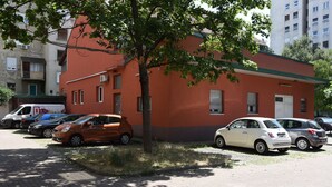 Un estacionamiento con varios coches, un árbol y un edificio de fachada roja.