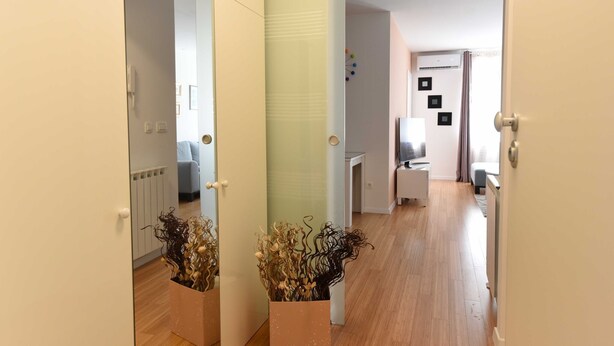 Un pasillo con piso de madera que conduce a una sala de estar con sofá y una mesa. Hay dos plantas en macetas en el pasillo.