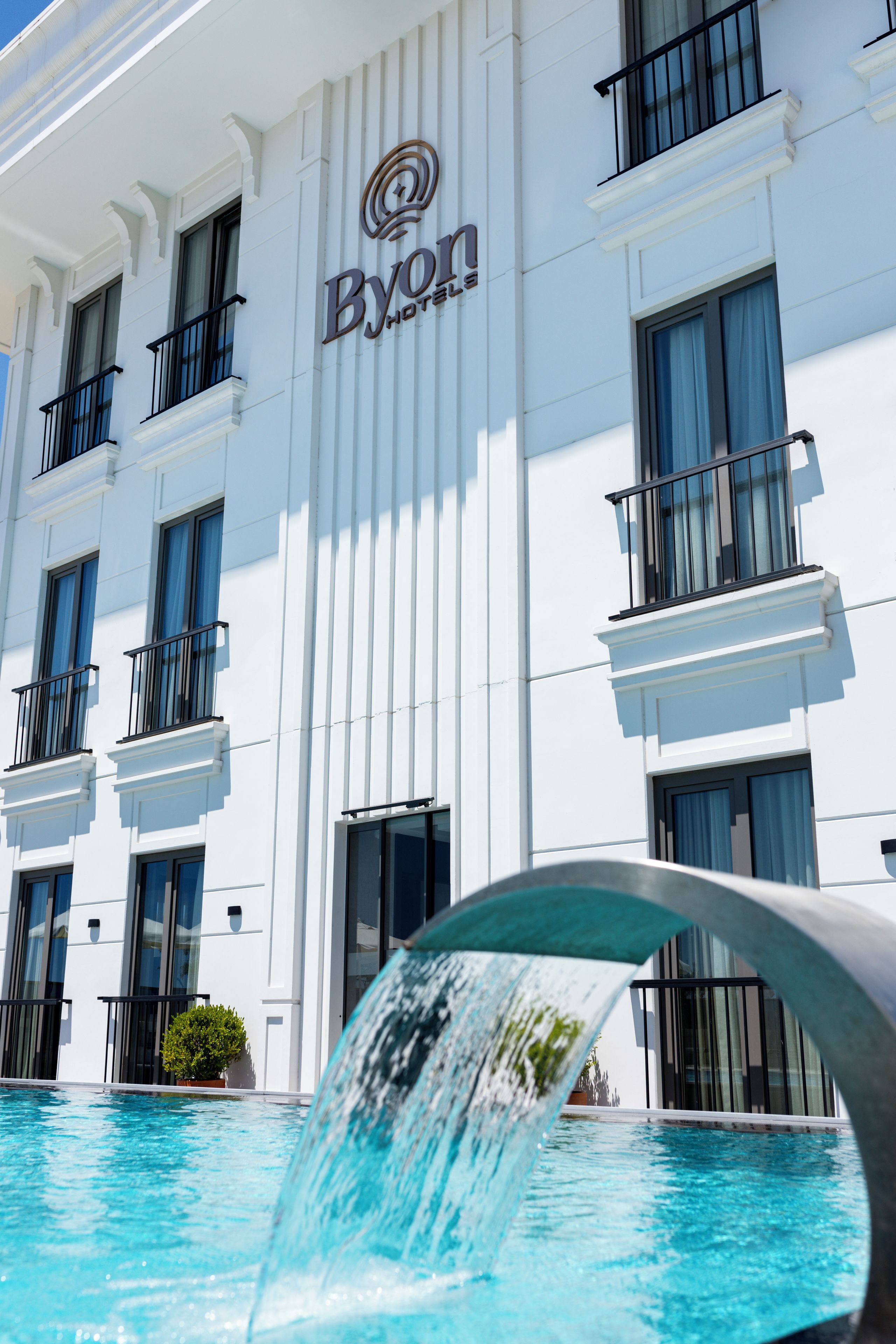 A hotel building with a sign reading 'Byon Hotels' and a swimming pool in the foreground.
