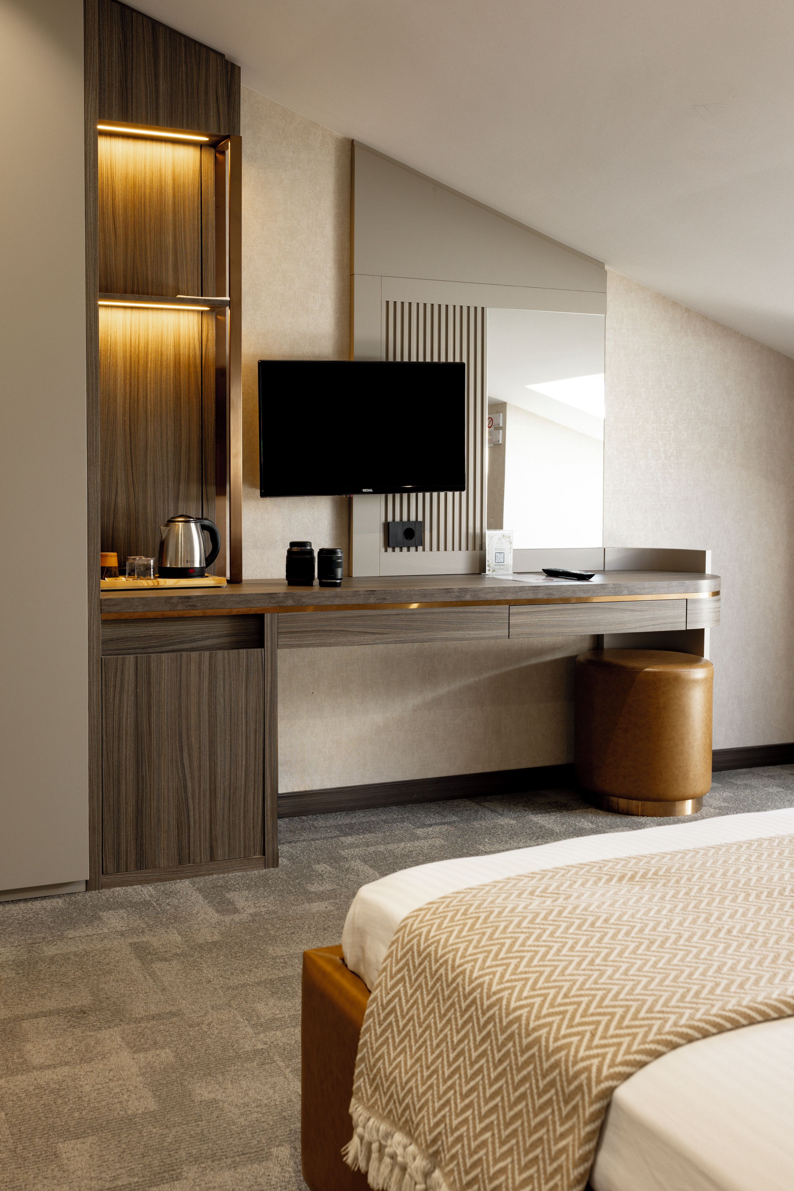 A modern hotel room with a large bed, a flat-screen TV, a coffee maker, and a wooden desk.