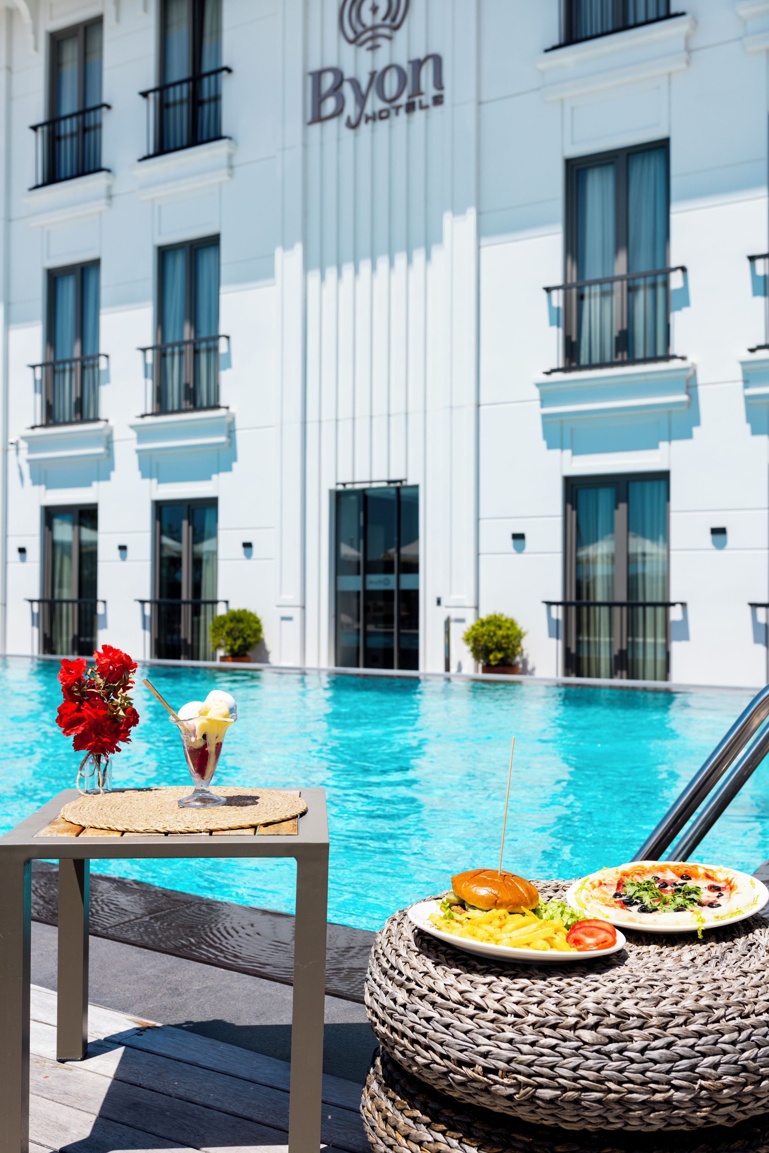 A poolside view with a dining table, a dessert, and a plate of food.