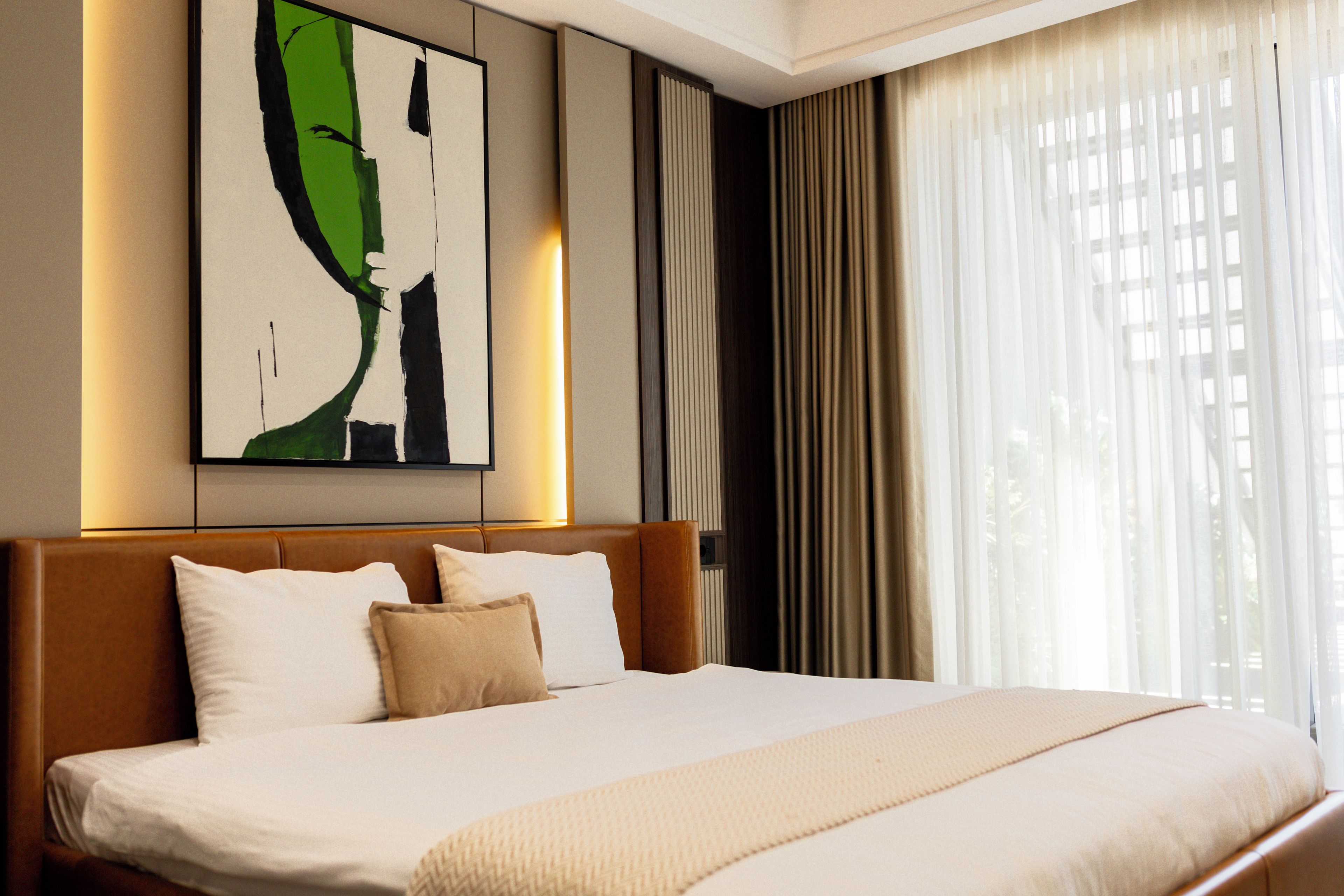 A hotel room with a large bed, a headboard, a wall-mounted artwork, and a window with curtains.