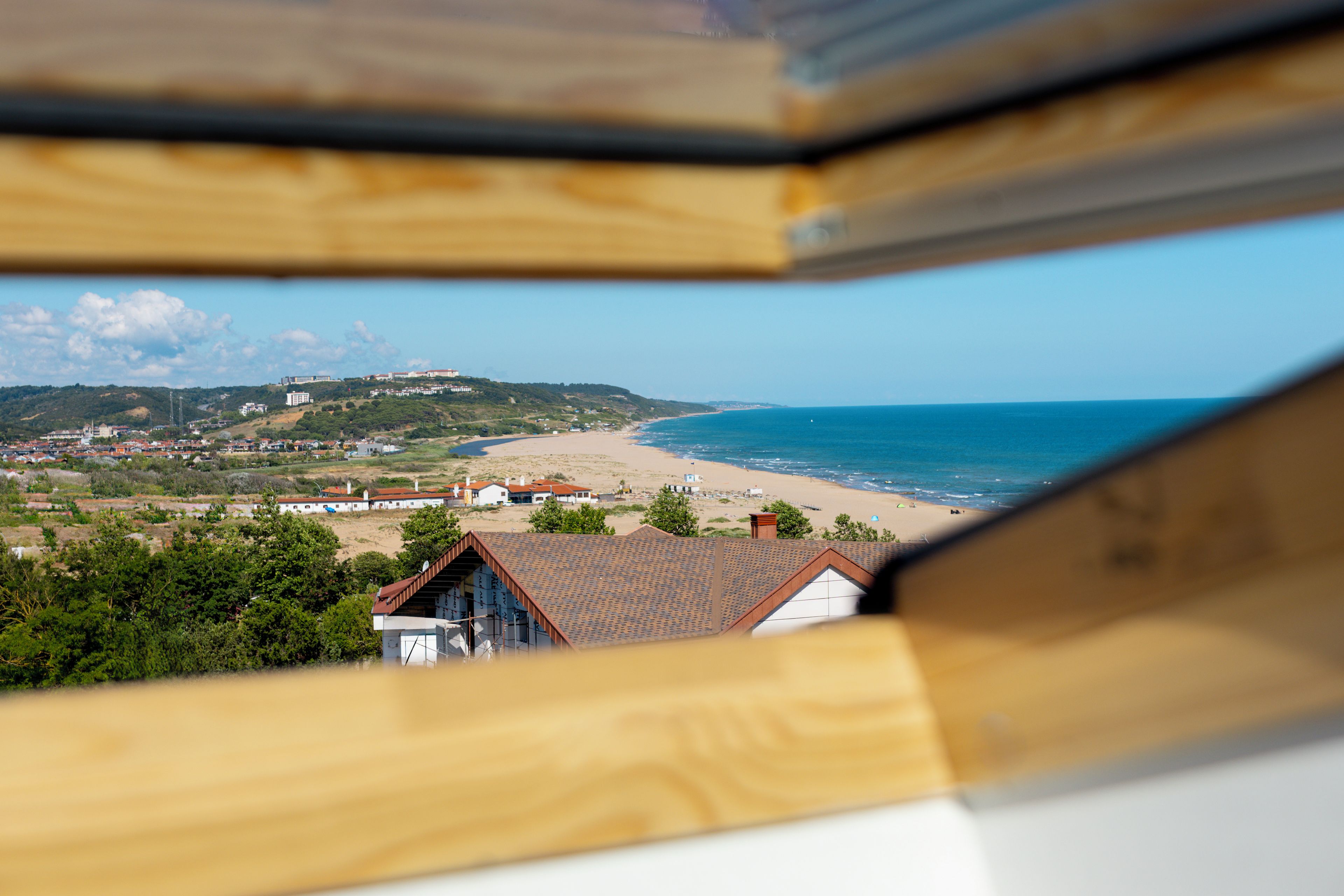 A coastal view with a beach, houses, and a hill with buildings.