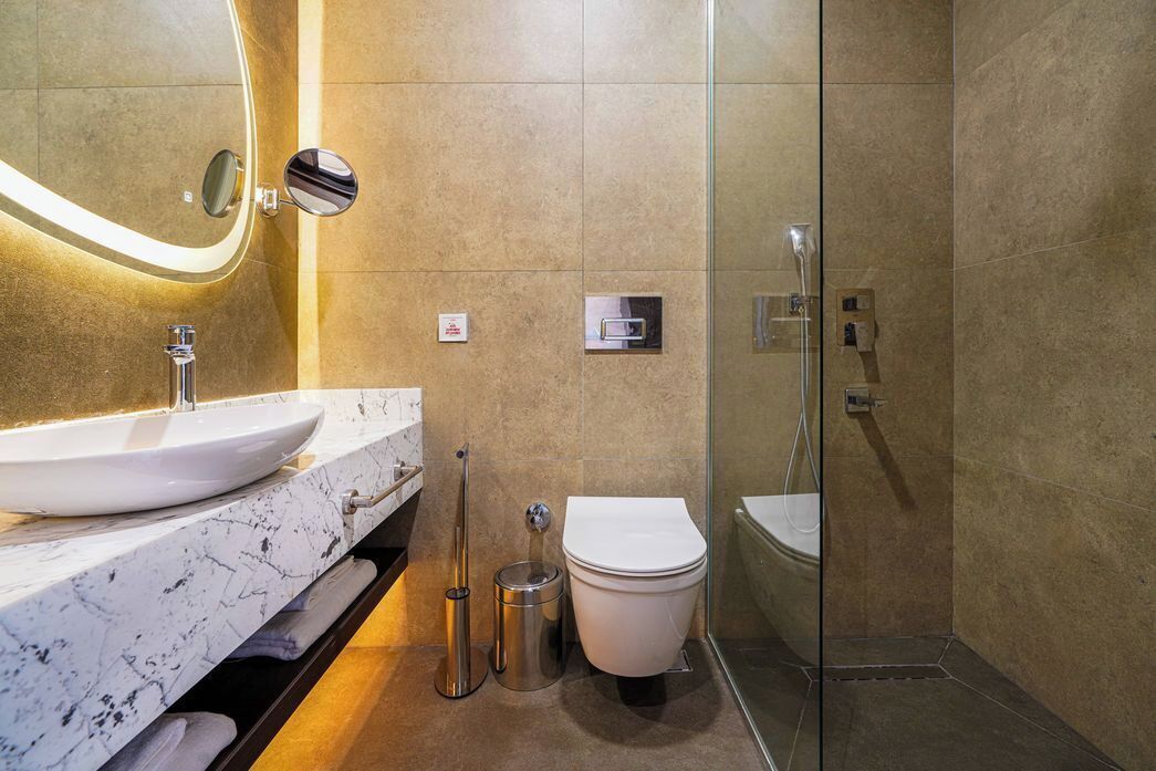 A modern bathroom with a marble sink, a toilet, and a glass-enclosed shower.