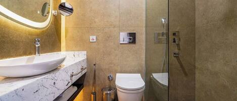 A modern bathroom with a marble sink, a toilet, and a glass-enclosed shower.