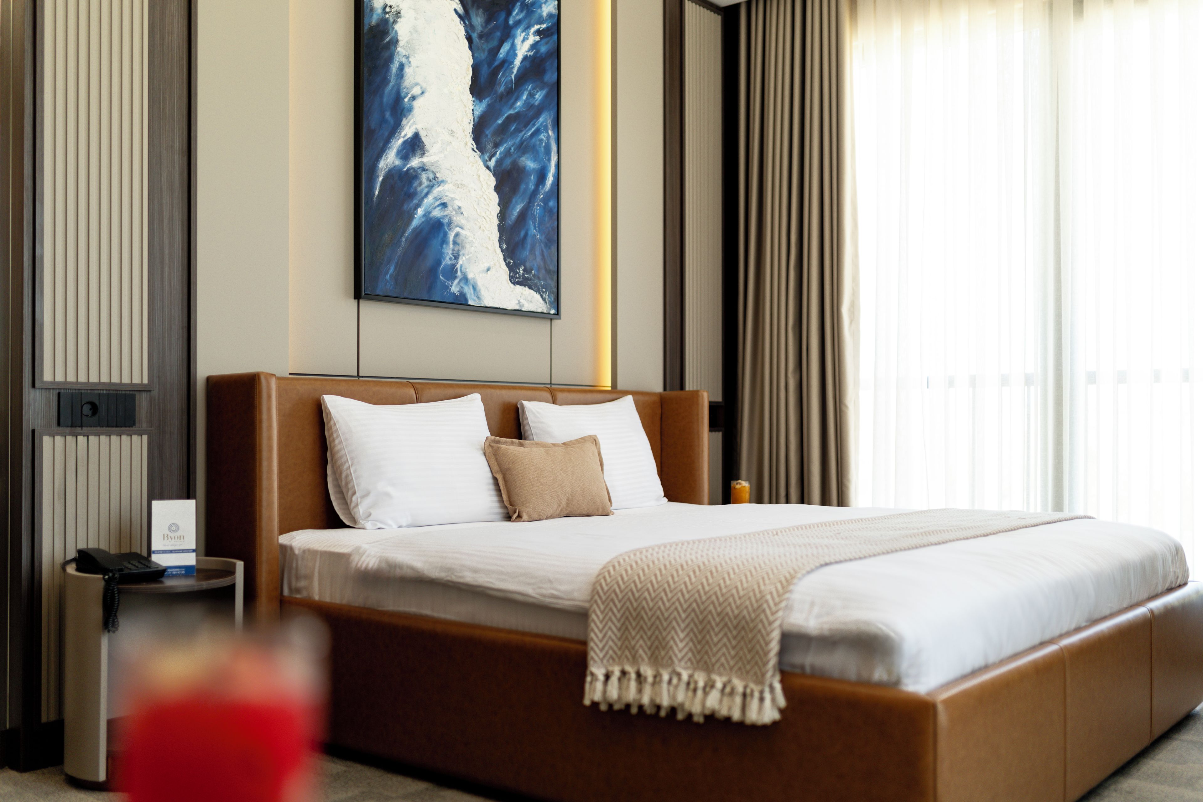 A hotel room with a large bed, a bedside table with a phone, and a painting on the wall.