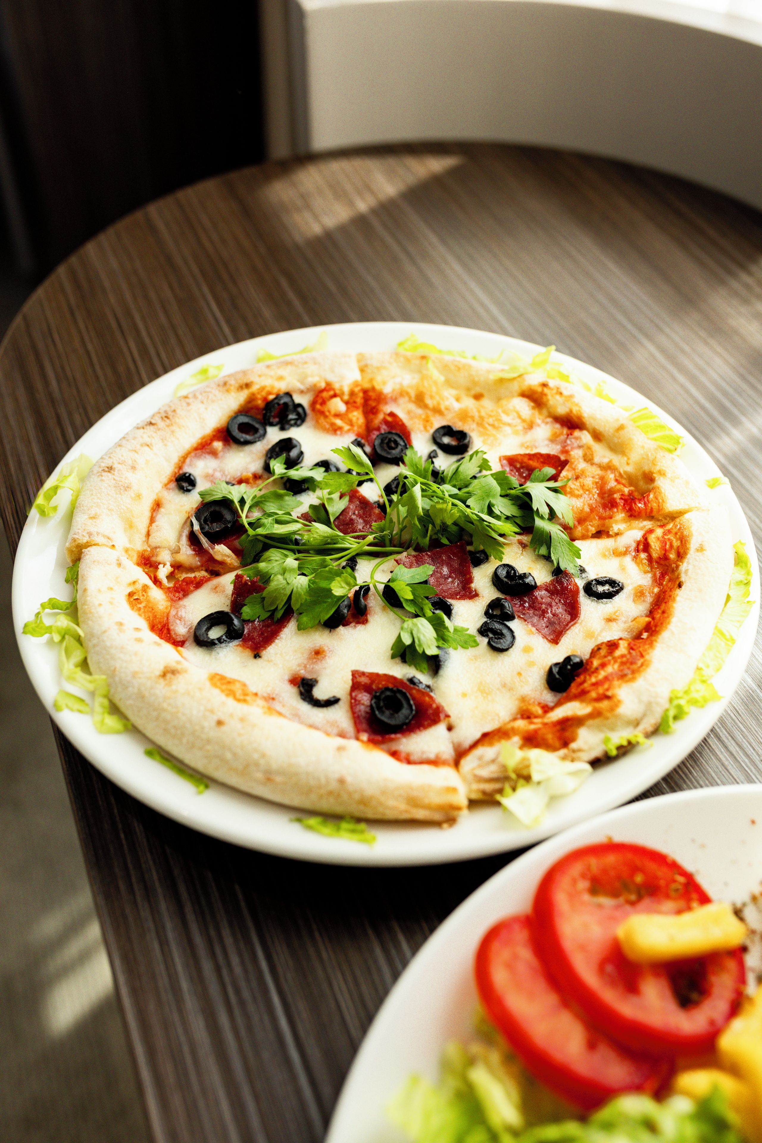 A pizza on a white plate with toppings on a wooden table.