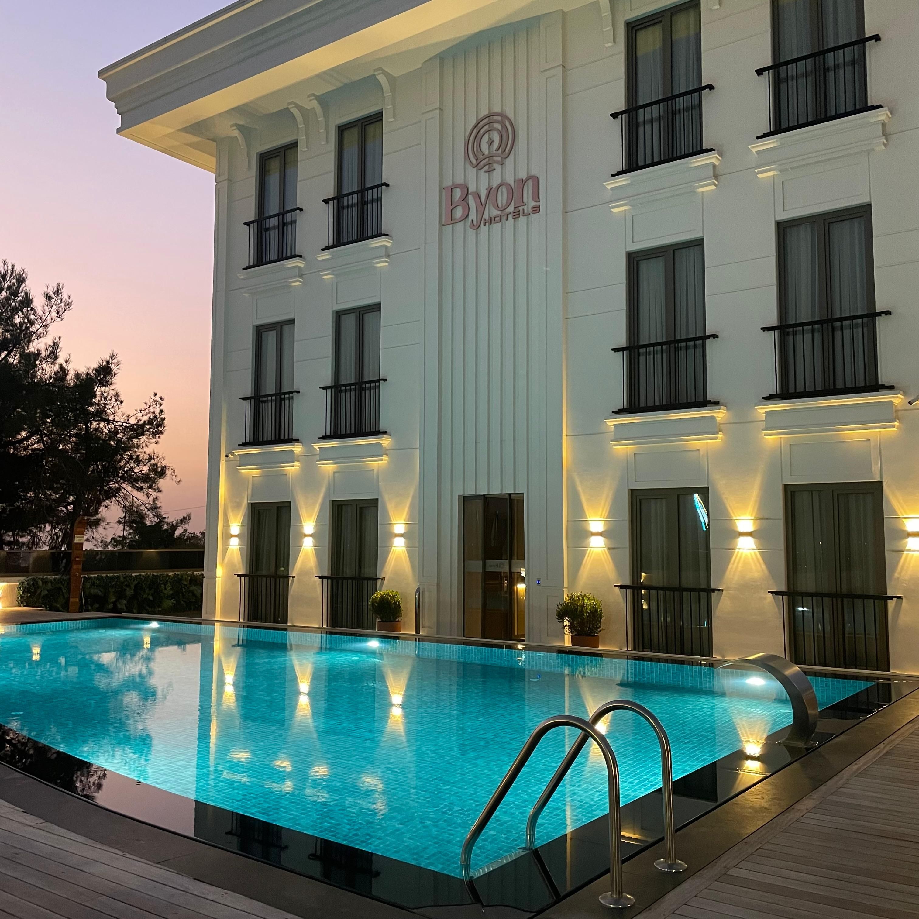 A hotel with a swimming pool, multiple balconies, and a sign reading 'Byon Hotels'.
