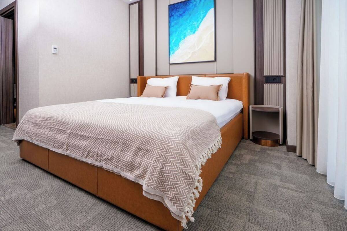 A modern hotel room with a large bed, a side table, and a painting on the wall.