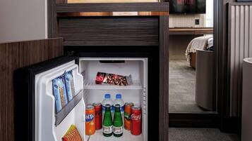 A compact kitchenette with a built-in refrigerator containing snacks and beverages.