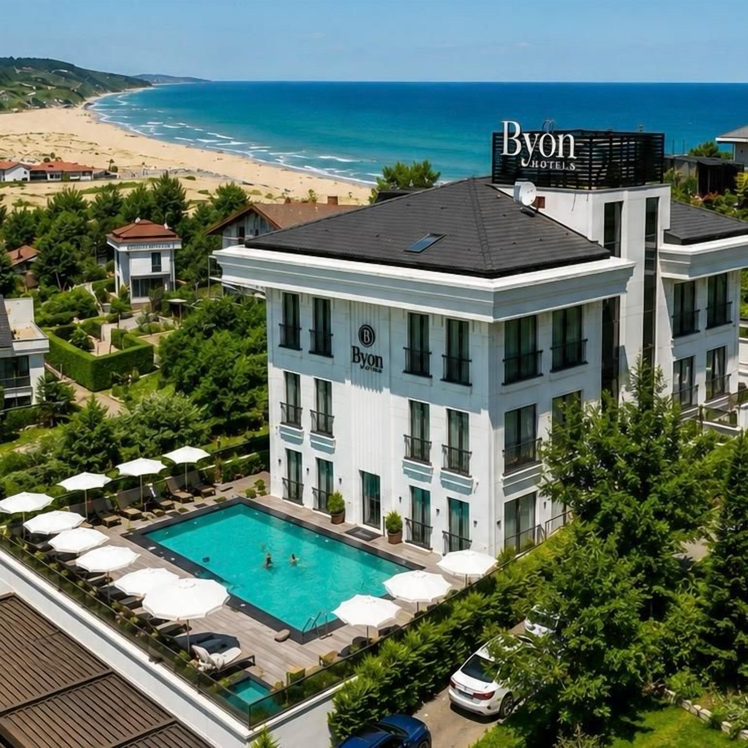A hotel with a rooftop pool, surrounded by lush greenery, and a view of the beach.