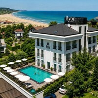 Um hotel com piscina no terraço, cercado por vegetação exuberante e vista para a praia.