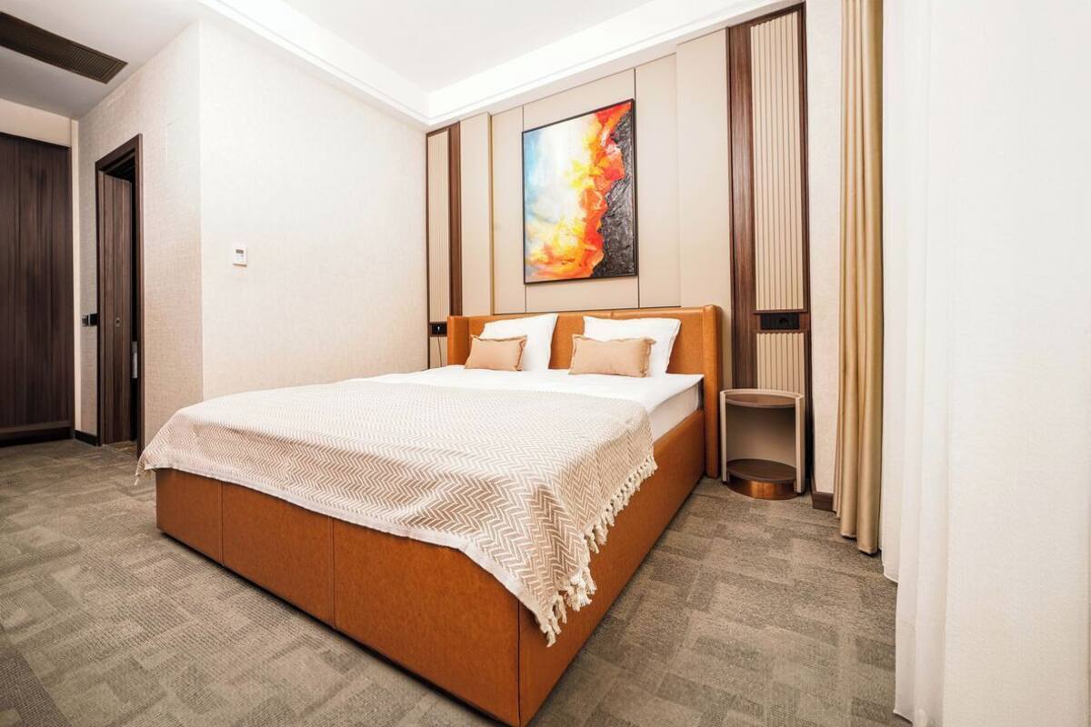 A hotel room with a large bed, a painting on the wall, and a small side table.