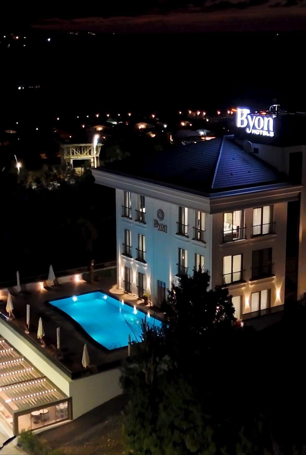 A hotel with a pool, a sign reading 'Byon Hotels,' and a well-lit exterior.