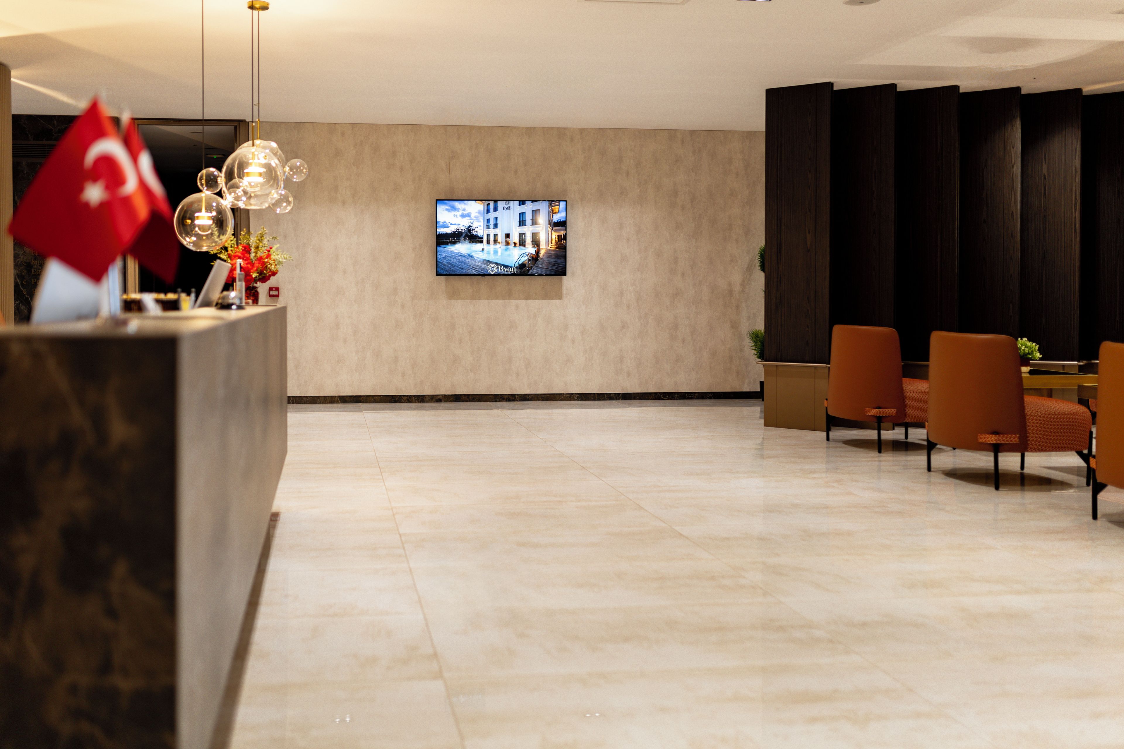 A hotel reception area with a reception desk, a television screen, and a seating area with chairs.