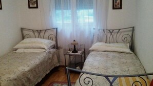 Una habitación con dos camas individuales, una mesita de noche con lámpara y una ventana con cortinas translúcidas.