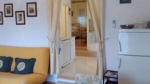 Una habitación con un sofá amarillo, una mesita, una cama y un área de cocina pequeña.