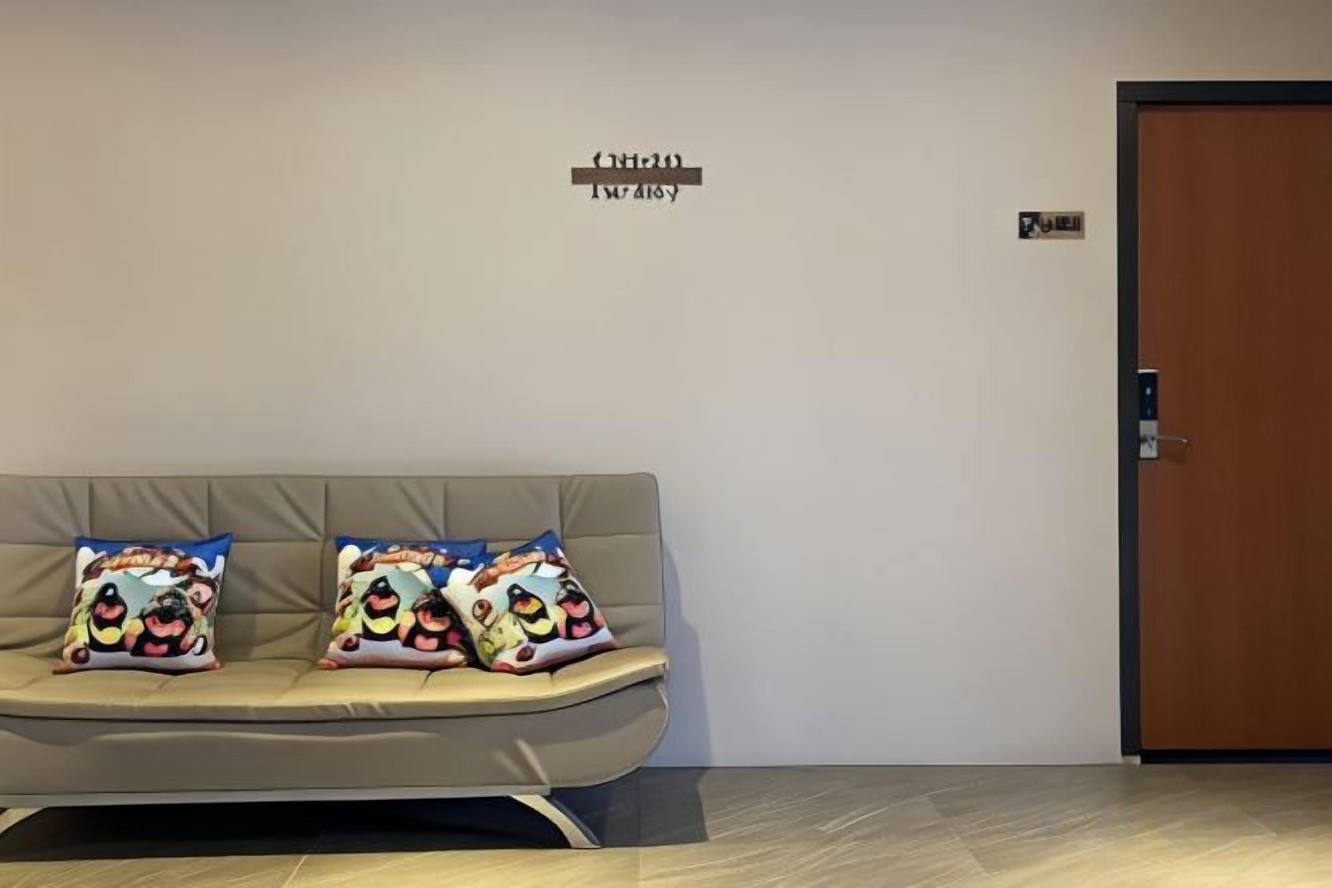 Un área de recepción con un sofá y dos almohadones, una puerta y un cartel en la pared.