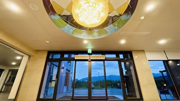 A hotel entrance with a large, illuminated spherical light fixture above the doors, a red welcome mat, and a view of the outdoors through the glass doors. - Mizuho Hotel (Hualien)