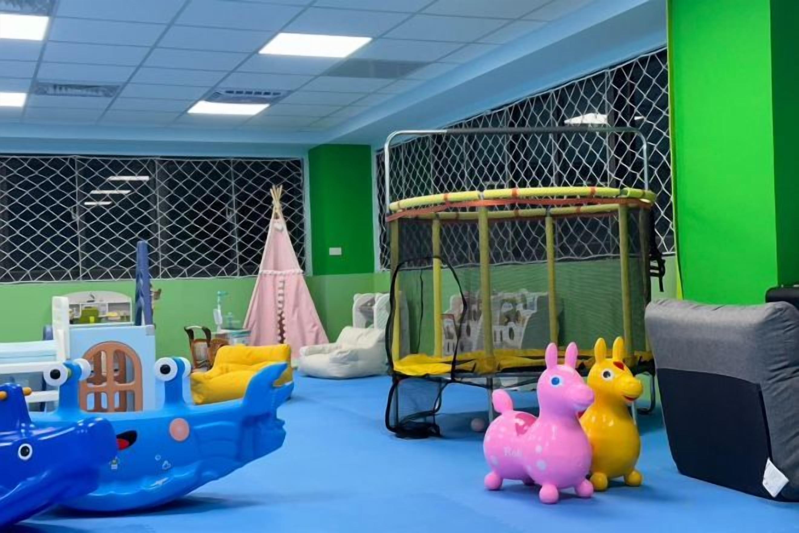 A play area with a blue boat, a pink and yellow toy horse, and a trampoline.