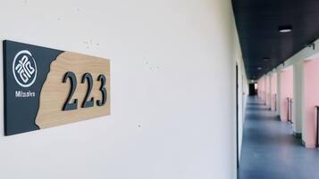 Un pasillo con una señal indicando la habitación 223, un logotipo y una vista parcial de un corredor con puertas.