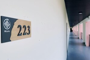 Un pasillo con una señal indicando la habitación 223, un logotipo y una vista parcial de un corredor con puertas.