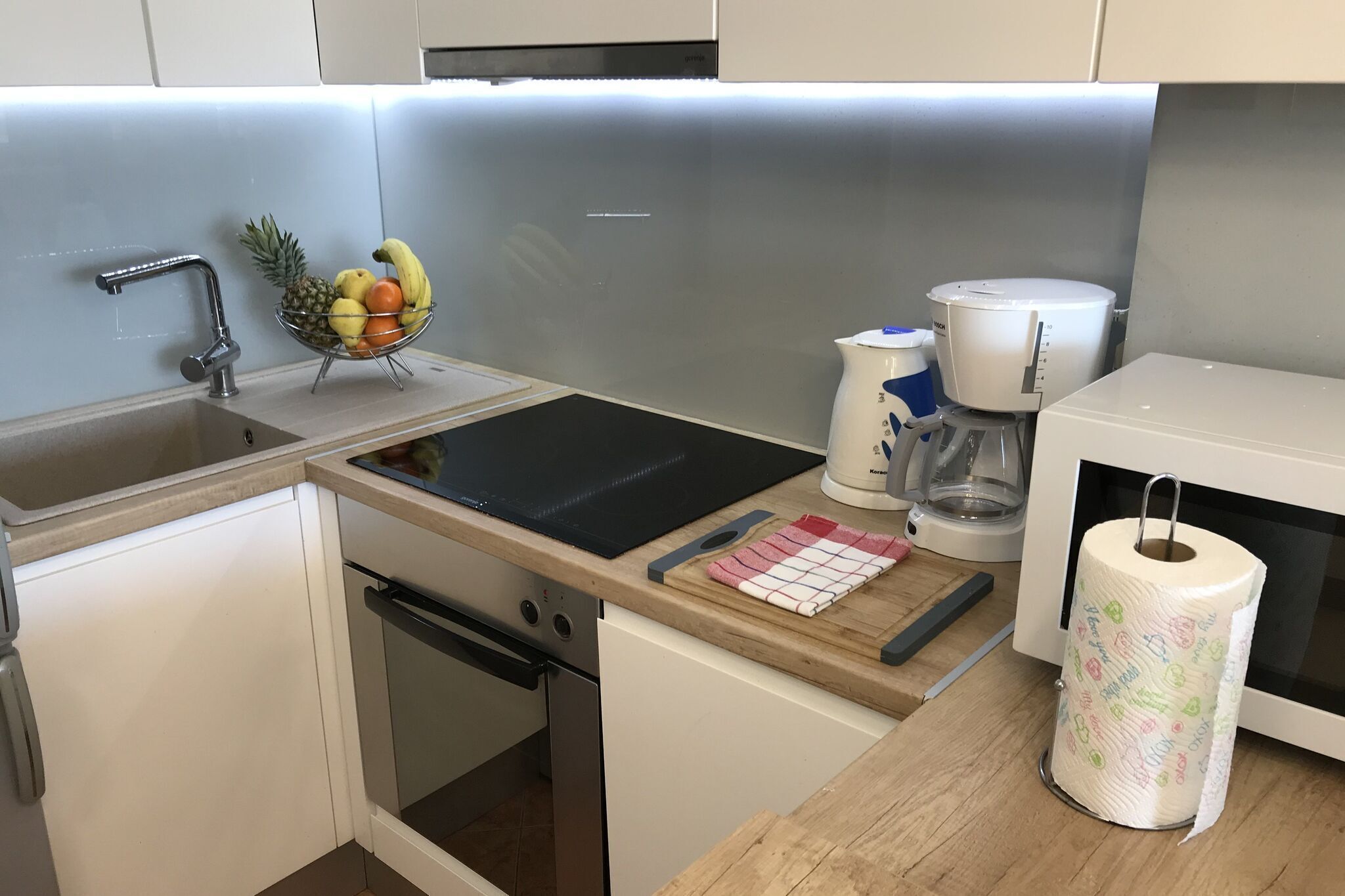 A modern kitchen with a stainless steel sink, a fruit bowl, a coffee maker, and a microwave.