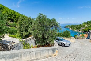 A coastal property with a car parked on a paved area, surrounded by greenery and a view of the sea.