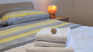 Una cama bien hecha con una colcha estampada, una pila de toallas blancas y una lámpara de noche.