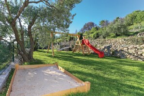 Une aire de jeux avec un toboggan et des balançoires, entourée d’une pelouse et d’arbres.