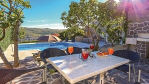 Un área de comedor junto a la piscina con mesa, sillas y vista a una piscina y montañas.