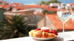 A croissant with strawberries and macarons on a plate, a glass of white wine, and a scenic view of buildings and the sea. - Apartments Villa Angela - Studio Apartment with Terrace and Sea View (Angela) (Baška Voda)