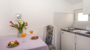 A small kitchenette with a sink and a window above it. There is a table with a vase of flowers, a glass of orange juice, and a plate of food. - Apartments Villa Angela - Studio Apartment with Terrace and Sea View (Angela) (Baška Voda)