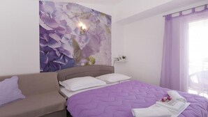 A bedroom with a bed, a sofa, a wall with a floral mural, and a window with purple curtains. - Apartments Villa Angela - Studio Apartment with Terrace and Sea View (Angela) (Baška Voda)