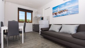 Eine moderne Küche mit weißen Schränken, einer Mikrowelle und einem Kühlschrank. Es gibt einen Esstisch mit Stühlen und ein Sofa im Wohnbereich.