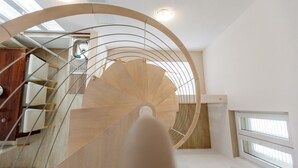 A modern spiral staircase with wooden steps and metal railings, leading to an upper floor.