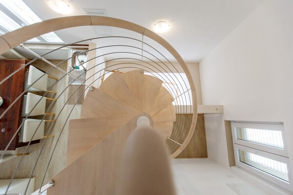 A modern spiral staircase with wooden steps and metal railings, leading to an upper floor.