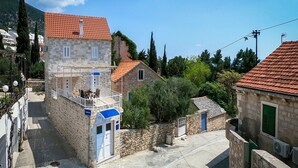 A stone building with a red-tiled roof, a small balcony, and a blue awning.