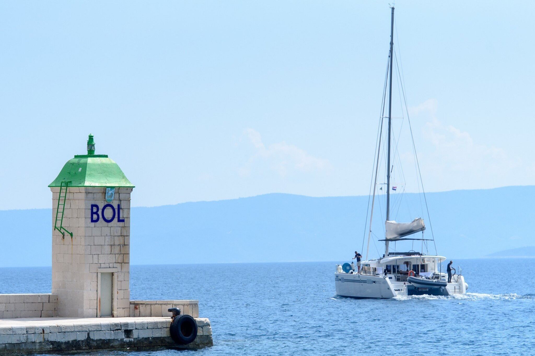 A lighthouse labeled "BOL" with a clear view of the sea and a sailboat in the background.